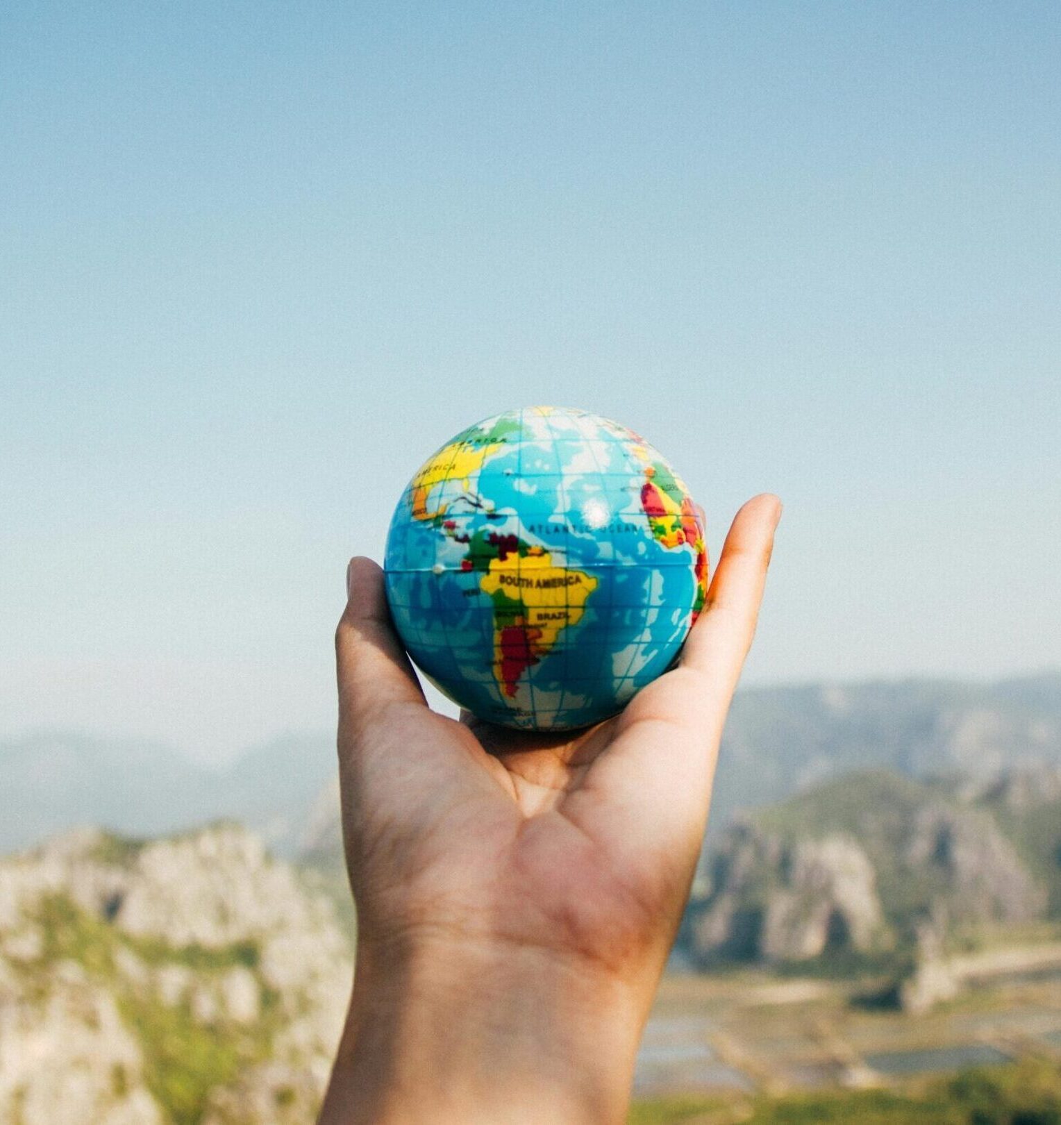 Hand holding a globe against a mountain background symbolizing travel and exploration.