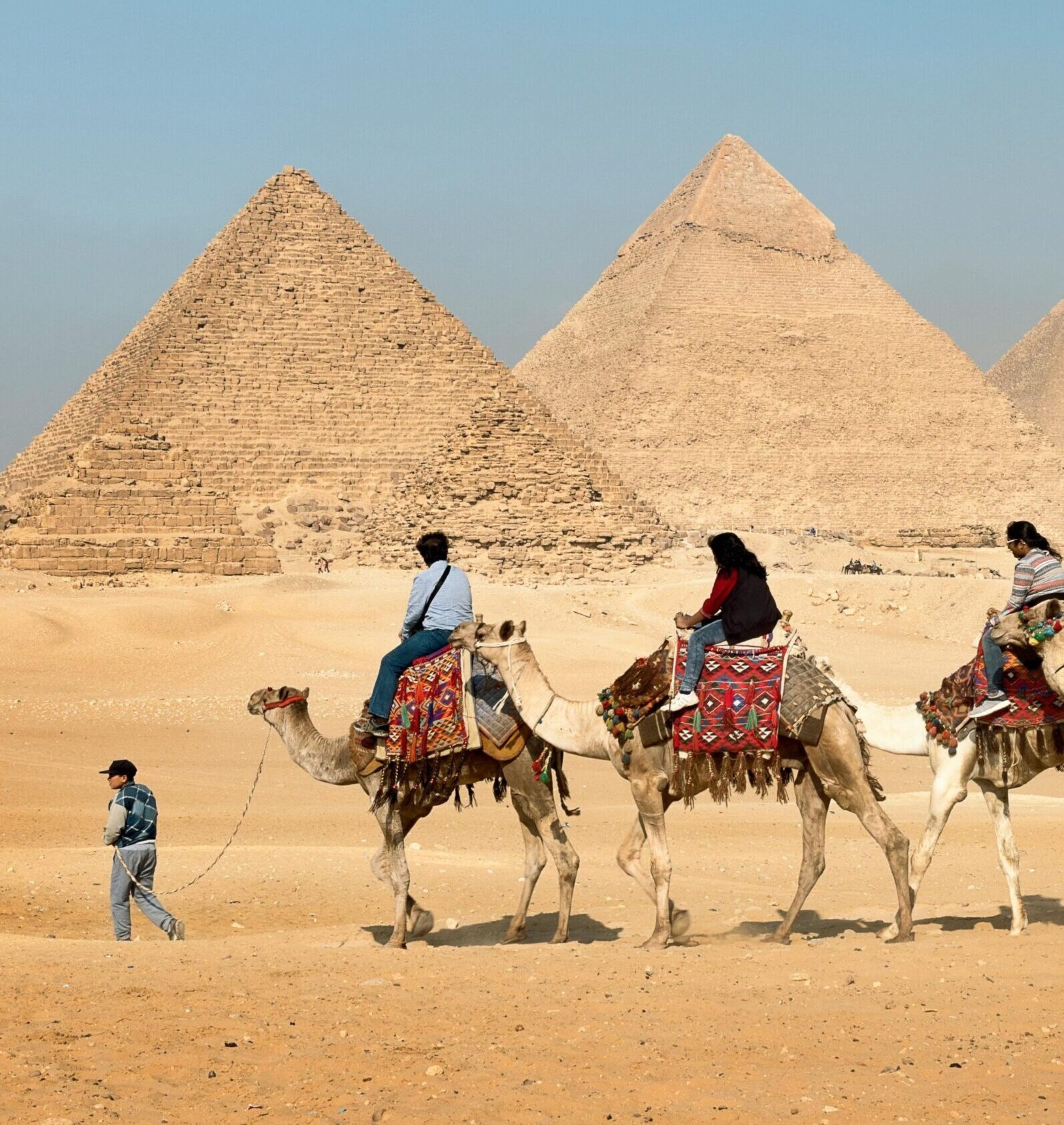 Tourists riding camels near the Great Pyramids of Giza, Egypt under clear skies.