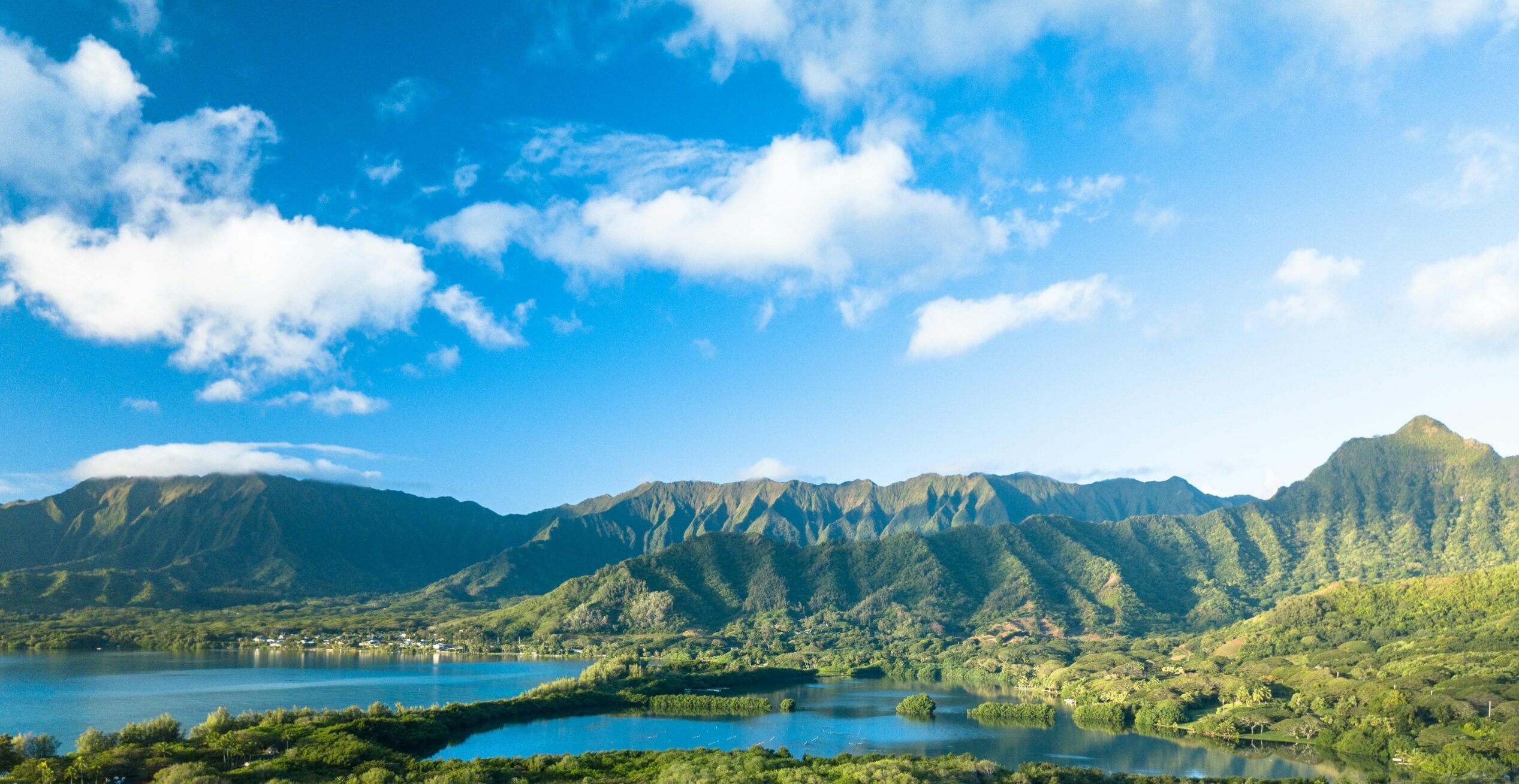 Scenic view of lush mountains and a lake under a bright blue sky with clouds.
