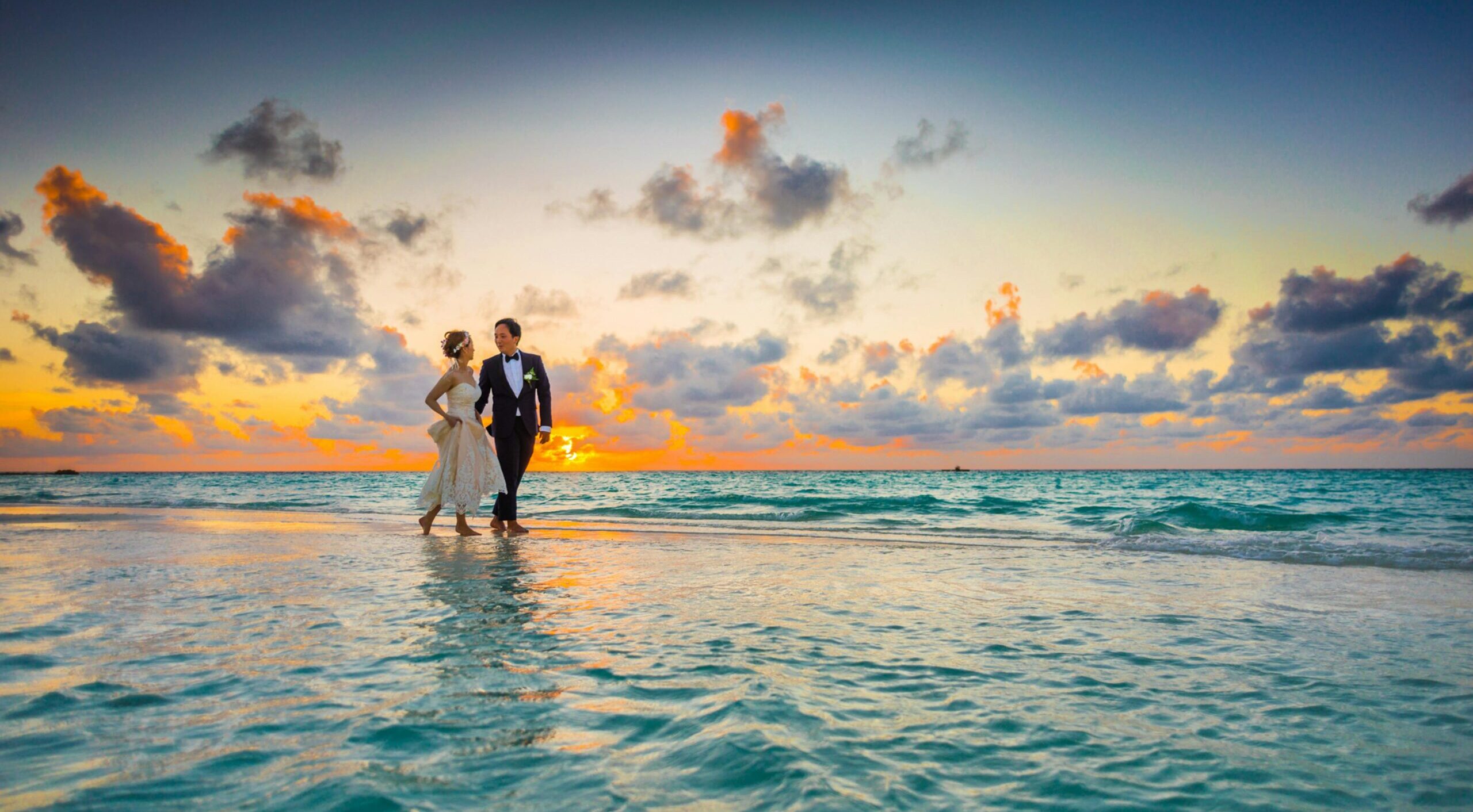 A young couple enjoying a romantic beach wedding during a vibrant sunset.